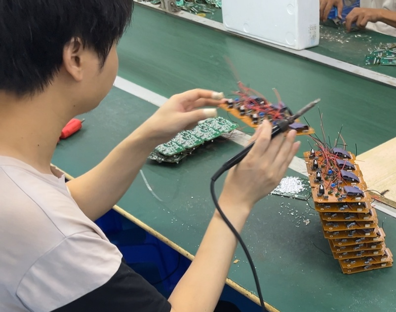 Skilled technician soldering electronic PCB components on hotel telephone production line